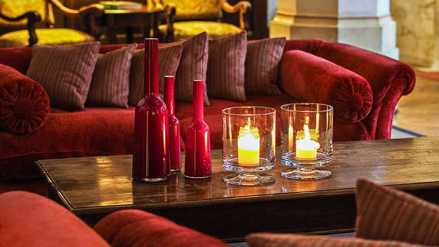 Gemütliches Wohnzimmer mit roten Sofas, dekorativen roten Flaschen und brennenden Kerzen auf einem hölzernen Couchtisch lädt Sie ein, Entspannung pur zu genießen.